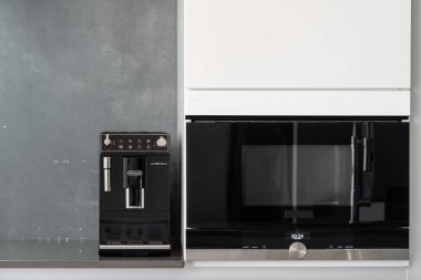 Kontrol düğmeli farklı düğmeleri olan siyah mikrodalga fırını olan beyaz dolap, zaman ve modu gösteren bilgi ekranı, mutfak tezgahında kahve yapma makinesi.