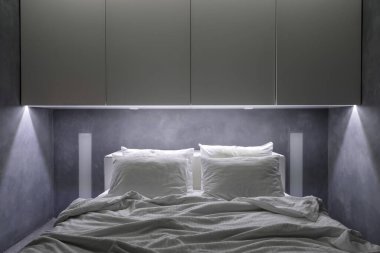 Otelde, evde ve farklı konaklama şekillerinde sağlıklı uyku kavramı. Beyaz gardırobun altında buruşmuş battaniyeyle rahat bir yatak. Minimalist yatak odalı modern dairede dolaplar.