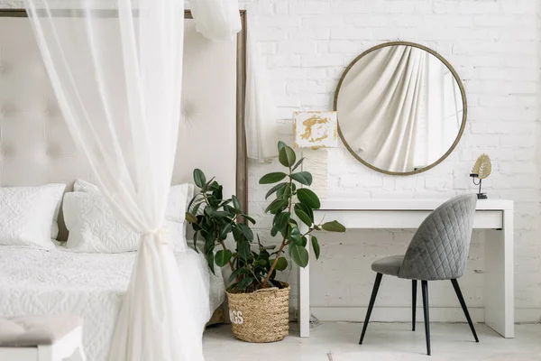 Ev yatak odası, daire tasarımı. Masanın yanında beyaz bir yatak, İskandinav tarzı ev mobilyaları. Aynalı minimalist ev dekorasyonu, ev bitkisi.