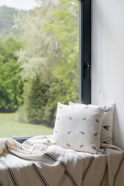 Pencereli, ev tasarımlı bir ev. Salonda kimse yok, rahat ev için modern dekorasyon. İskandinav konforlu dairesi. Yastığın dikey yakın çekimi, pencere pervazında battaniye.