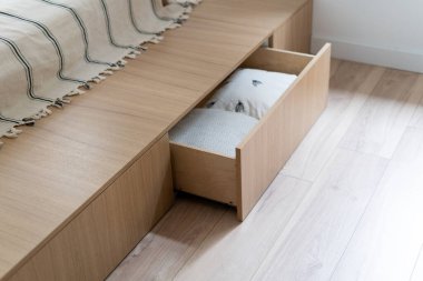 Yatak odasının içi, modern odada ahşap yatak. Açık ahşap çekmeceli mobilya tasarımı, kutuda beyaz yastık dekorasyonu nesnesi. Yatak yastığı için kahverengi konforlu depo.