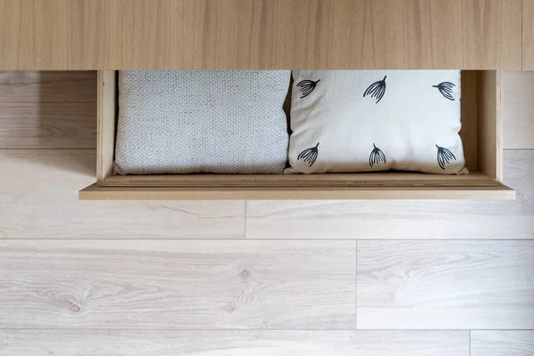 Home interior with wooden furniture, pillow in drawer. Cushion decoration at wood box, indoor design of modern apartment. Closeup to scandi bedroom cabinet, comfortable white object.