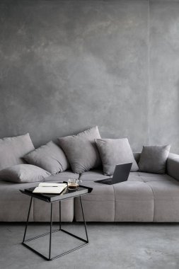 İş seyahati ve uzaktan çalışma konsepti. Ev ofisindeki rahat koltukta modern dizüstü bilgisayarın dikey görüntüsü. Açık kitaplı kahve masası ve çatı katı tarzlı bir dairede sıcak bir bardak içecek.