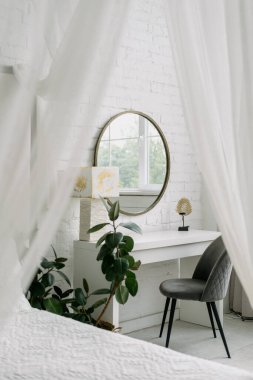 Yatak odasının içi, beyaz oda tasarımına yakın çekim. Evde kimse yok, İskandinav apartman dekorunun dikey görüntüsü. Perdeli mobilyalar, masa, ayna, yatağın yanındaki sandalye..