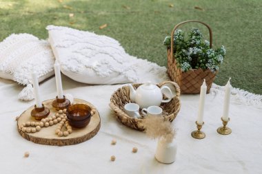 Yeşil çimlerde beyaz battaniye, piknik için açık hava dekorasyonu. Yastıklar, bulaşıklar, yaz parkında ahşap süslemeler. Dışarıda kimse yokken dekoratif kırsal şeylere yakın çekim..