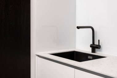 Mutfak iç mimarisi, modern ev tasarımına yakın çekim. Çağdaş ev odasında siyah lavabo, beyaz tezgahta temiz çelik musluk. Kirli ev detaylarıyla minimalist daire biçimi.