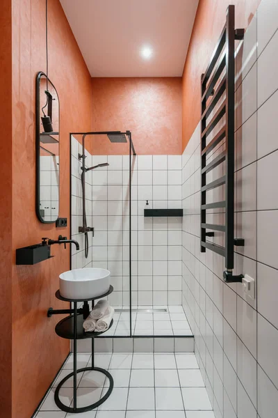 Modern bathroom interior, vertical shot of home design. Contemporary apartment with minimalistic style shower, nobody at room with faucet, sink and mirror. Black modern furniture indoors.