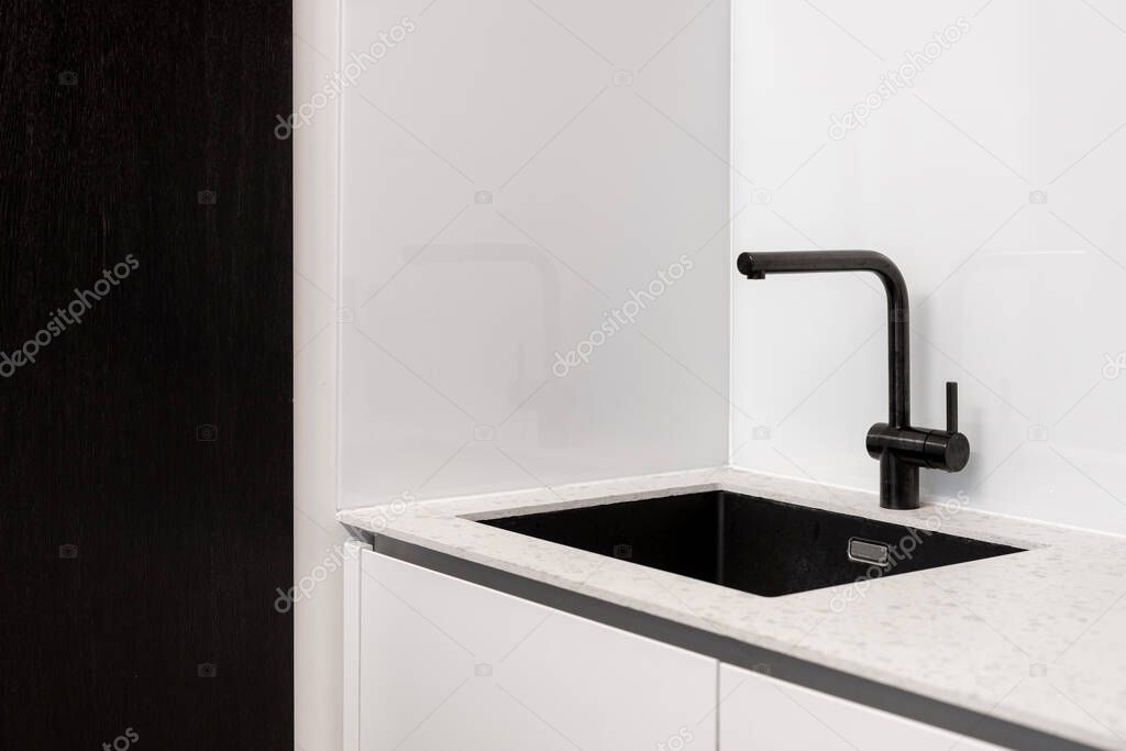 Kitchen interior, closeup at modern home design. Black sink at contemporary house room, clean steel faucet at white counter. Minimalistic apartment style with chrome domestic details.