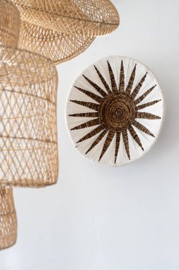 Ev dekorunun dikey görüntüsü, beyaz fotokopi duvarında asılı doğal malzemeler, bohem stili, el yapımı hasır abajur yanında.