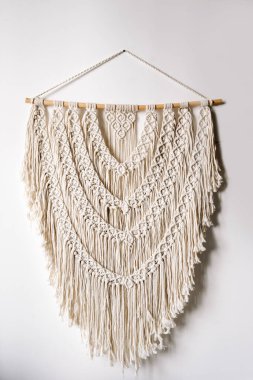Parlak odadaki beyaz duvarda ahşap bir tahtada asılı duran el yapımı makramin dikey görüntüsü. Boho tarzı örgü ve iplik ev dekorasyonu kavramı
