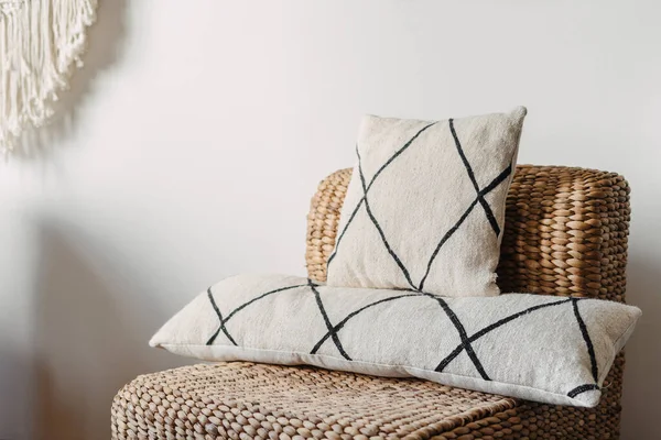 Close up view on soft cushions on comfortable wicker armchair in hygge house. Living room with ethnic boho interior, home decor and rattan furniture against white copy space wall