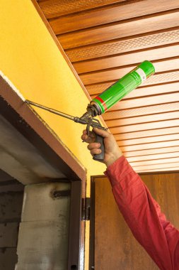 Construction builder works with polyurethane foam during frame insulation at door installation clipart