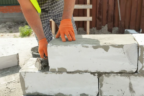 Maurer Mann Arbeiter in orangefarbenen Handschuhen installiert belüfteten Block mit Kelle — Stockfoto