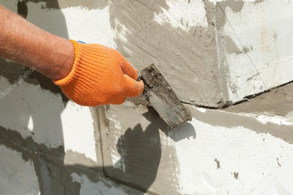 Bricklayer man worker in orange gloves installing aerated block with trowel