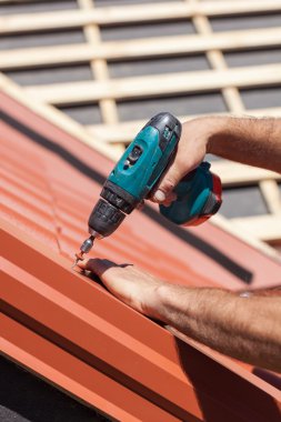 Elektrikli matkap yükleme kırmızı metal bir çatı üzerinde çalışan döşeme ahşap ev