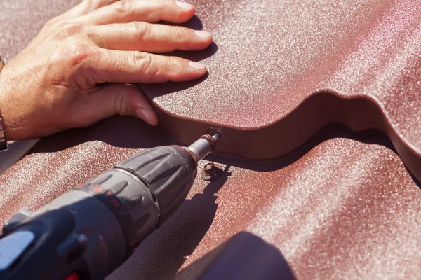 Arbetare på ett tak med borrmaskin installera röd metall plattor på trähus — Stockfoto