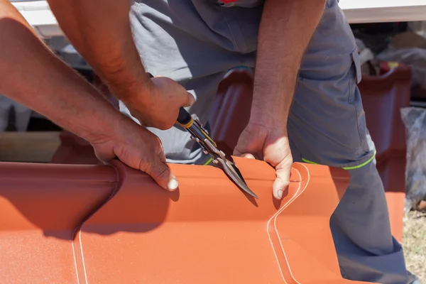 Roofers cut a metal tile using cutting pliers