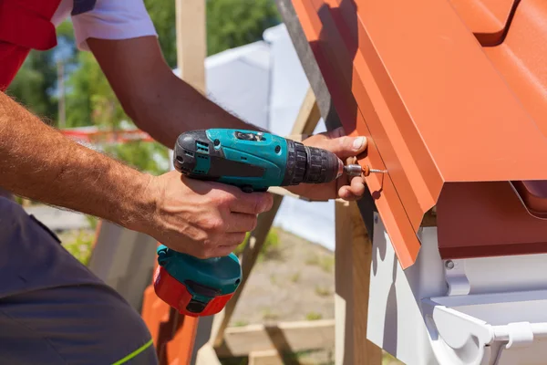 Travailleur sur un toit avec perceuse électrique installant des tuiles métalliques rouges sur une maison en bois — Photo