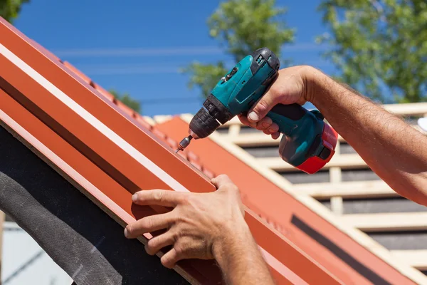 Arbetare på ett tak med borrmaskin installera röd metall plattor på trähus — Stockfoto