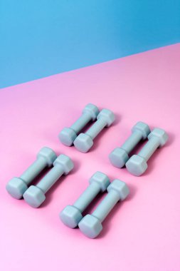 Açık mavi halterler pembe ve mavi arka planda uzanıyor, sağlık ve zindeliği destekliyor. Ev eğitimi için ideal ağırlıklar fiziksel aktiviteyi ve egzersiz rutinlerini geliştirir..