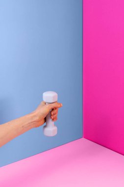 Bir el canlı pembe ve mavi bir arka plana karşı hafif bir halter tutar, ev çalışma potansiyelini vurgular. Bu düzen spor meraklıları ve yeni başlayanlar için idealdir..