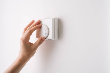 Bir el, modern bir yerleşim yerindeki konfor ve enerji verimliliği aletlerine odaklandığını gösteren şık bir dairedeki minimalist bir duvarın termostatını ayarlar..