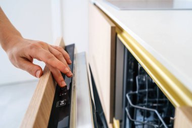 Bir el, gösterişli, çağdaş bir bulaşık makinesinin kontrollerini minimalist bir mutfakta ayarlar. Bu cihaz modern evlerde bulaşık yıkama görevlerinin basitleştirilmesinde hayati bir rol oynar..
