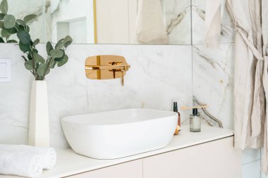 Sakin bir banyoda parlak beyaz bir lavabo ve şık bir musluk bulunur. Samimi alan, yumuşak ışıklandırma ve minimalist dekorla geliştirilmiş sabah rutini boyunca kendine bakımı davet eder..