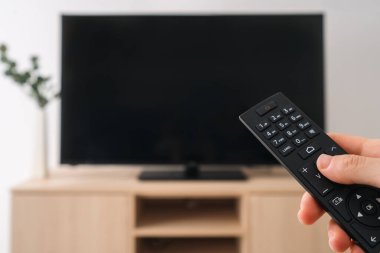 Uzaktan kumandayı tutan bir el, bu rahat dairede film gecesine hazır. Programı seç, kanalı değiştir, televizyonu kapat. Ahşap bir dolaba monte edilmiş parlak LCD televizyonlu oturma odası.