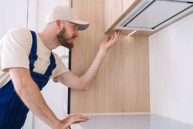 Garanti hizmeti konseptleri. Tamirci, mobilyaların içine yeni bir mutfak dolabı, kurşun ışık ve fırın kaputu monte etmeye odaklanmış durumda. Ev eşyaları olan bir apartman dairesi.