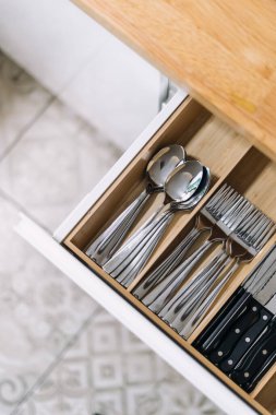 Modern bir mutfak çekmecesi işlevsellik ve tasarımı vurgulayan çatal bıçak ve çatal bıçaklarla dolu düzenli bir alan sergiliyor. Temiz yemek kaşıkları, çatallar ve bıçaklar tahta kutuda, dikey atış.