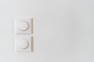 Beyaz fotokopi duvarındaki iki yuvarlak ışık anahtarının yakın çekim görüntüsü, parlak oturma odasındaki enerji verimliliği elementlerine minimalist bir yaklaşımı vurguluyor