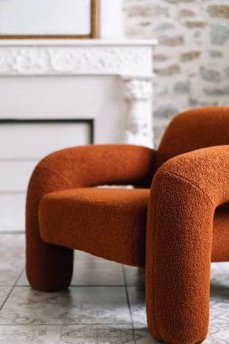 Oturma odasında yumuşak turuncu bir koltuk ve bulanık arka planda taş bir duvar sergileniyor. Doğal ışık, çağdaş mobilyalarla eski evdeki modern dekorasyon ve konut cazibesini arttırır.