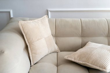 Bu davetkar yaşam alanı yumuşak, desenli yastıklarla süslenmiş şık beyaz bir kanepeyi gösteriyor. Minimalist tasarım, bir ev dekoru ve çağdaş konut ortamında rahatlığı vurgular.