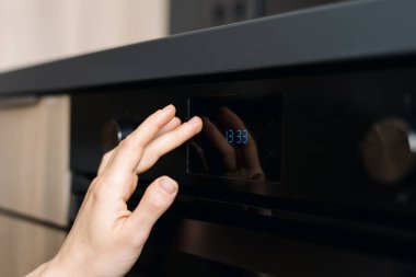 Bir el modern bir elektrikli fırının ayarlarını ayarlıyor. Ev aletleri çağdaş mutfakta. Gösterişli tasarım ve dijital ekran bu şık alanda yemek pişirme deneyimini artırır.