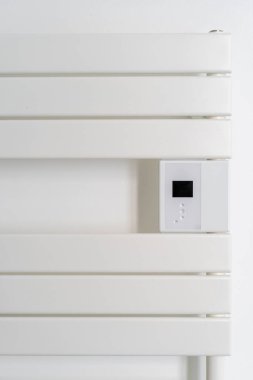 Duvara monte edilmiş beyaz bir radyatör ya da havlu ısıtıcısının modern tasarımı, kolay sıcaklık ayarları için entegre bir kontrol paneli içeriyor. Banyo içinde ev aletleri kavramları.