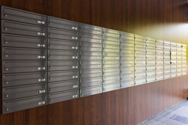 Sayısız metal posta kutusu güvenli bir şekilde bir apartman koridoruna yerleştirilerek posta dağıtımı ve yazışma tahsilatı için özel bir alan sunuluyor..