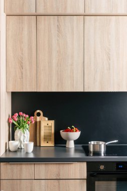 Çağdaş mutfak vitrinleri parlak siyah bir tezgah, ahşap bir kabin ve taze çiçekli canlı bir dekor ve bir kase çilek. Fonksiyonel ama şık bir yemek alanı.