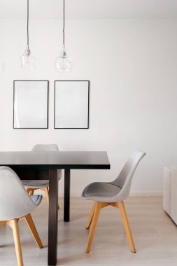 Beyaz duvardaki sanat eserlerini taklit et. Toplantı odasında fotokopi alanı olan çerçeveler. Yemek salonu olan dairede parlak siyah bir masa ve gri sandalyeler var. Yumuşak doğal ışık minimalist dekoru artırır