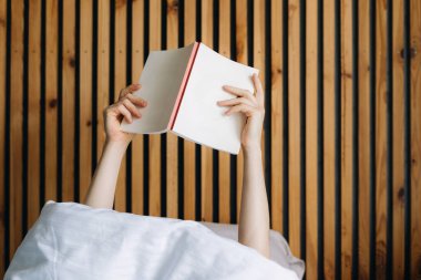 Şık bir otel odasında, misafir yorganın altında rahatlar, yatakta kitap okumaktan zevk alır. Sıcak tonlar ve ahşap aksanlar rahat atmosferi mükemmel bir konaklama için geliştirir..