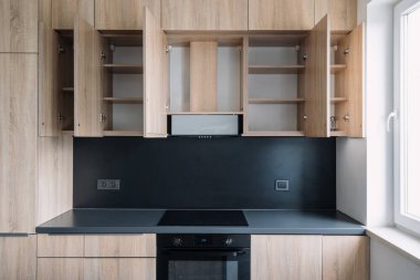 Bu modern mutfak ahşap dolaplar, açık kapılar ve boş raflar sergiliyor. Havalı, siyah bir tezgahın üstündeki depo. Parlak dizaynlı bir daire, yenilenmiş bir yer.