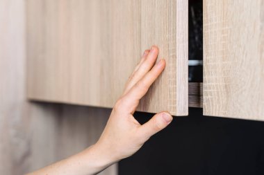 Modern mutfak iç mimarisi, özel yapım mobilyalar. Dairesinde bir dolabın ahşap kapısını açan kişi. Bir dolap veya deponun ılık tonları ve parlak tasarımı