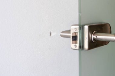 Kapıdaki kapı kolunun yakın görüntüsü alçı duvardaki hasara ve alçıpandaki deliğe, seçici bir şekilde probleme odaklanmış. Ev bakımı, yenileme, restorasyon yüzeyleri ve evde diy kavramı