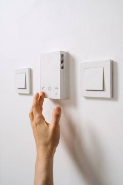 Intercom, sesli iletişim ve akıllı teknoloji kavramları. Bir el, kurye, misafir ya da ziyaretçi için konut kapısının açılması için çağdaş koridorda akıllı kontrol paneline uzanır..