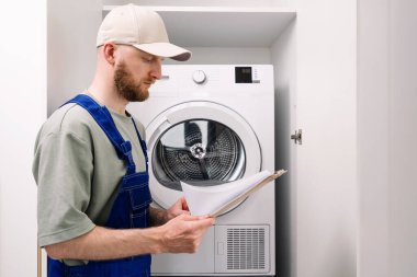Bir teknisyen, bir evin temiz çamaşır odasında çamaşır makinesini incelerken bakım yönergelerini gözden geçirir. Ev aletlerinin en iyi durumda tutulması üzerinde duruluyor..