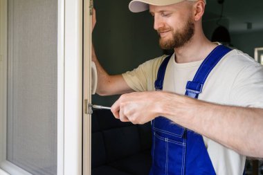 Bir tamirci, bir apartman dairesine PVC pencere çerçevesi kurmaya çalışıyor. Pencerenin optimal enerji verimliliği ve güvenliği sağlamak için bir tornavida kullanıyor..