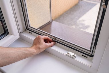 Bir tamirci pencere çerçevesinde böceklere karşı yeni bir cibinlik yerleştirir, yaz sezonuna hazırlanır, odayı havalandırır. Konut alanındaki rahatlık kavramları, kırpılmış bir el.