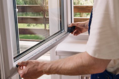 Tamirci, konut odasındaki bir pvc pencere çerçevesini ölçen bant kullanarak cibinlik ya da jaluzi takmaya hazırlanıyor. Ev rahatlığı kavramları