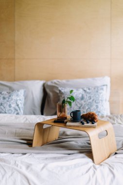 Yatak ve kahvaltı. Konforlu otel odasında rahat mobilyalar ve yumuşak yatak döşemeleri sergileniyor. Tahta tepside kahve ve kruvasan bulunur. Evde dinlenmek için ideal sakin bir atmosfer yaratır.