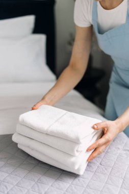 A hotel staff member meticulously arranges fresh towels on a neatly made bed in a stylish bedroom. The morning light enhances the inviting atmosphere of the room.